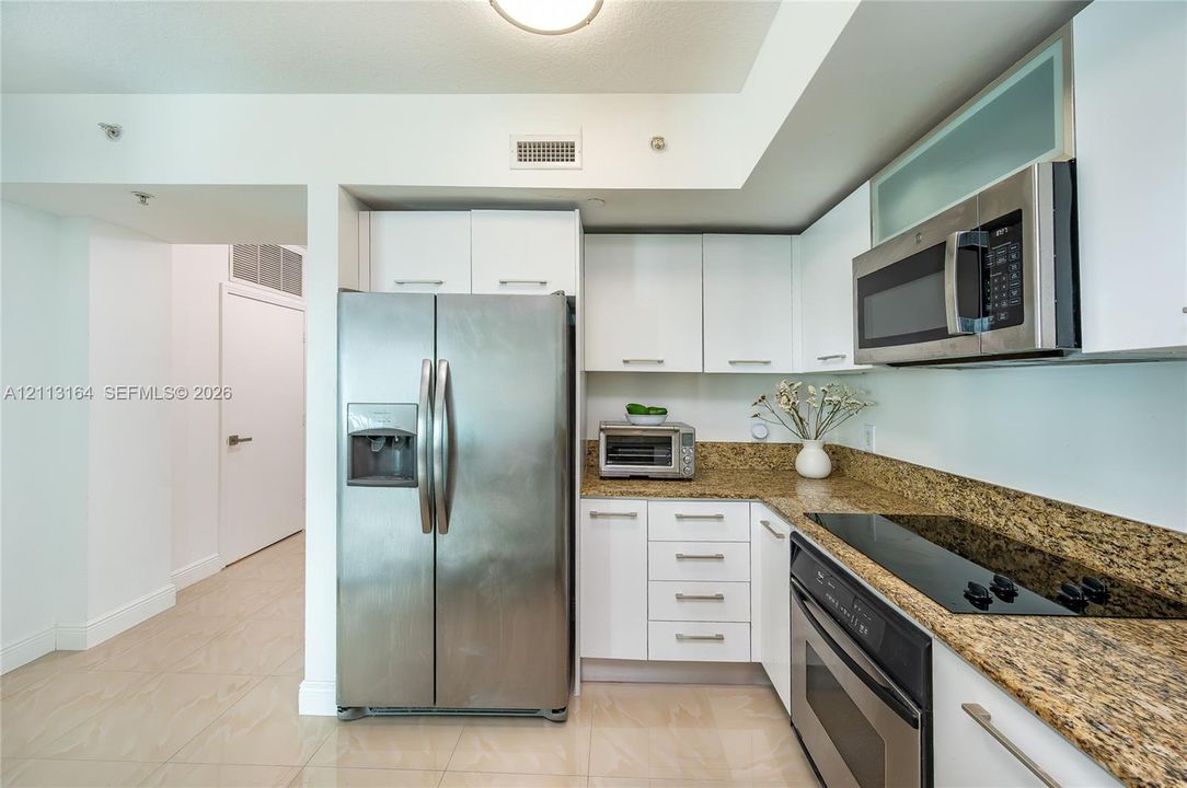 Kitchen featuring white cabinetry, stone countertops, stainless steel side-by-side refrigerator, built-in microwave, and integrated electric cooktop