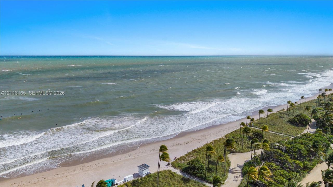 Coastal property featuring direct oceanfront access, sandy beach, paved pedestrian pathways, and mature coastal vegetation