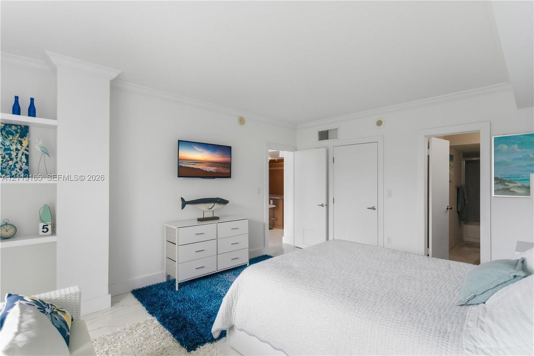 Room featuring crisp white walls, built-in shelving, crown molding, and neutral flooring