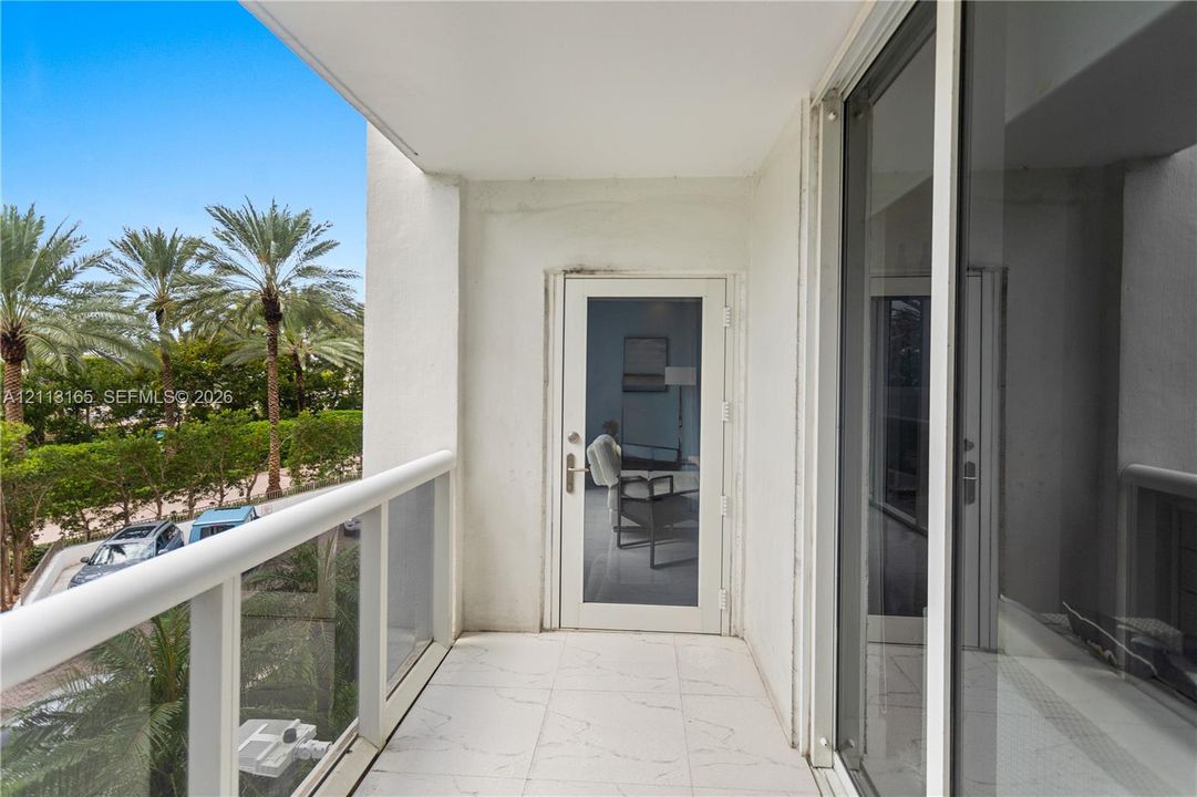 Covered balcony featuring white tiled flooring, a glass-panel railing, and a full-height glass entry door