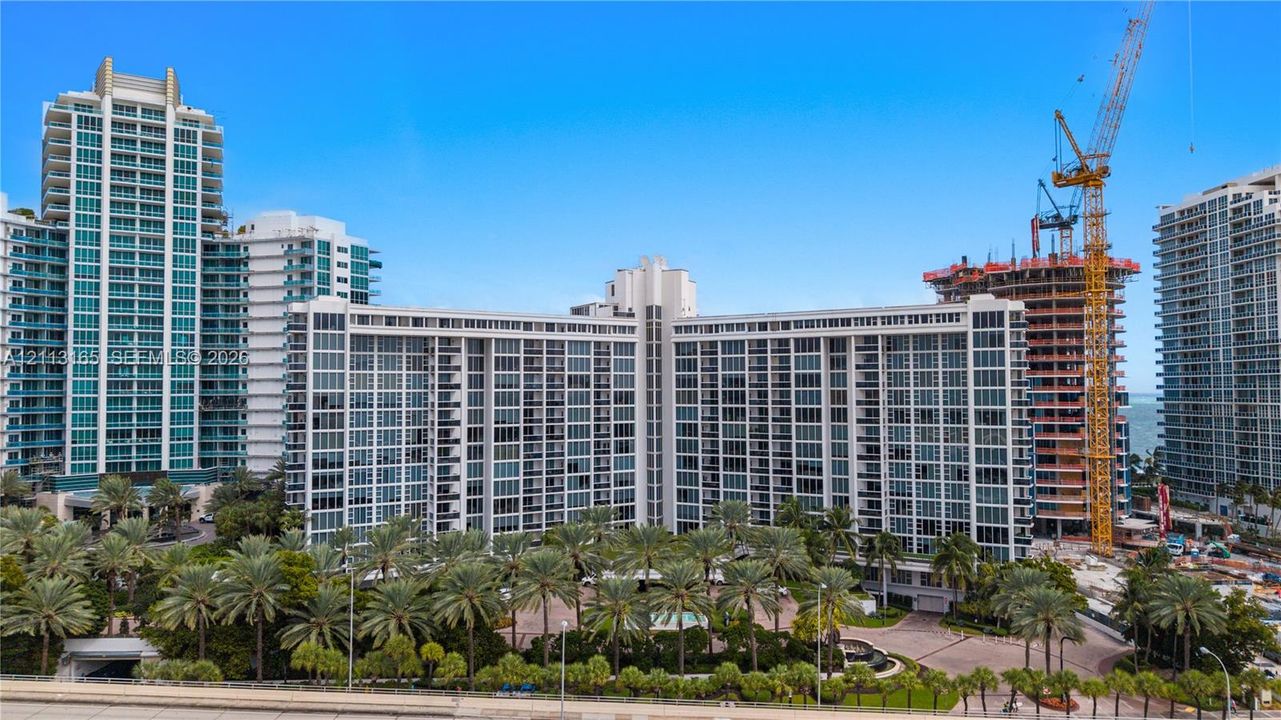 High-rise residential building featuring floor-to-ceiling glass paneling, extensive private balcony configurations, and landscaped grounds with mature palm trees