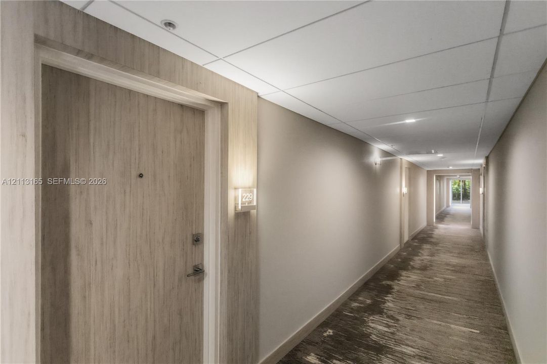 Interior hallway featuring wood-finish door cladding, recessed ceiling lighting, wall-mounted sconces, and patterned carpet flooring