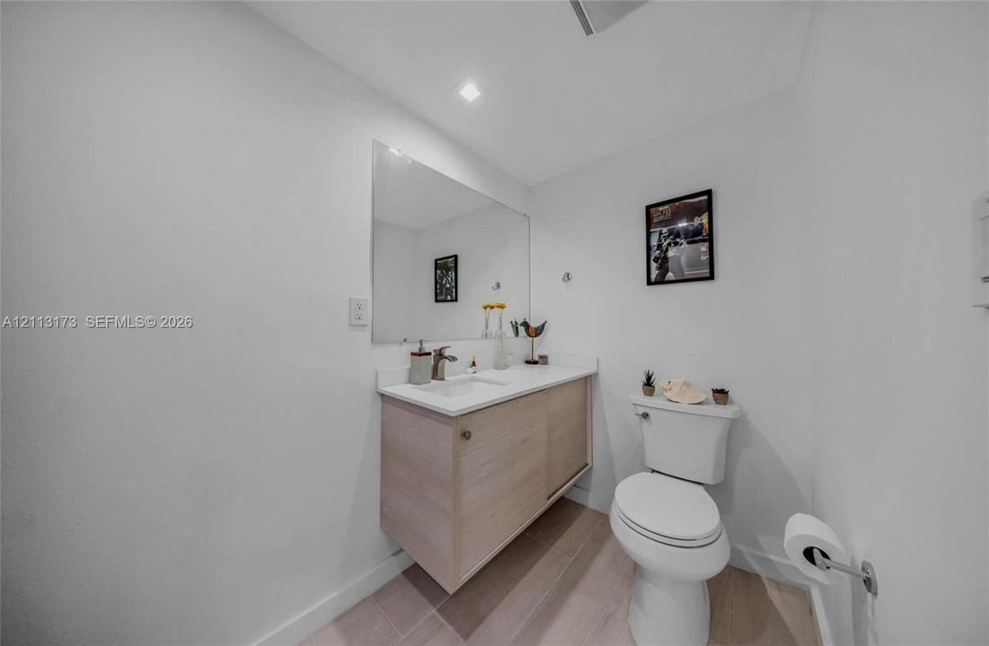 Floating vanity with a light wood finish, integrated white countertop with basin, wall-mounted mirror, recessed ceiling lighting, and neutral-toned flooring