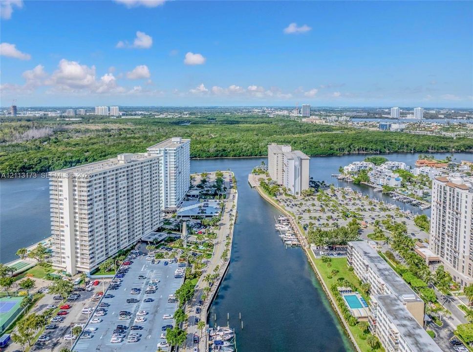 Aerial perspective featuring waterfront high-rise residential buildings, a central navigable waterway, on-site parking lots, and coastal landscaping
