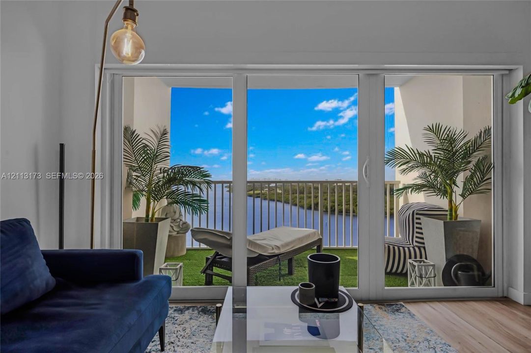 Large-format glass sliding doors opening to a private balcony with metal railing, synthetic turf flooring, and water scenery