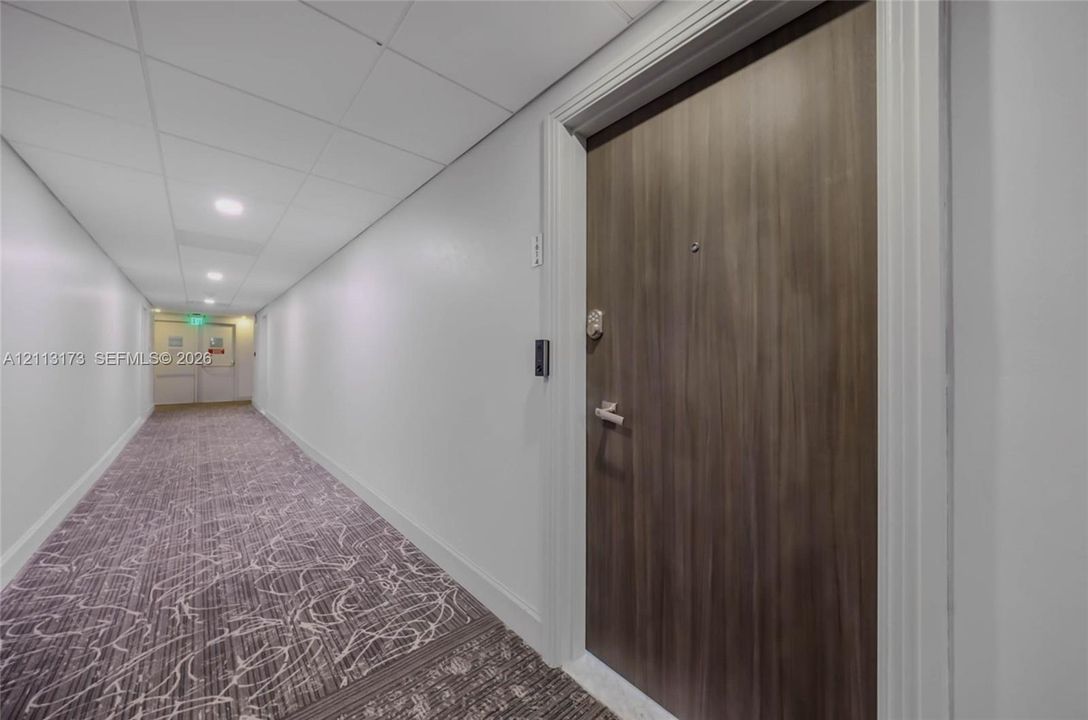 Wood-finish entry door with metal hardware, recessed ceiling lighting, and patterned carpeting