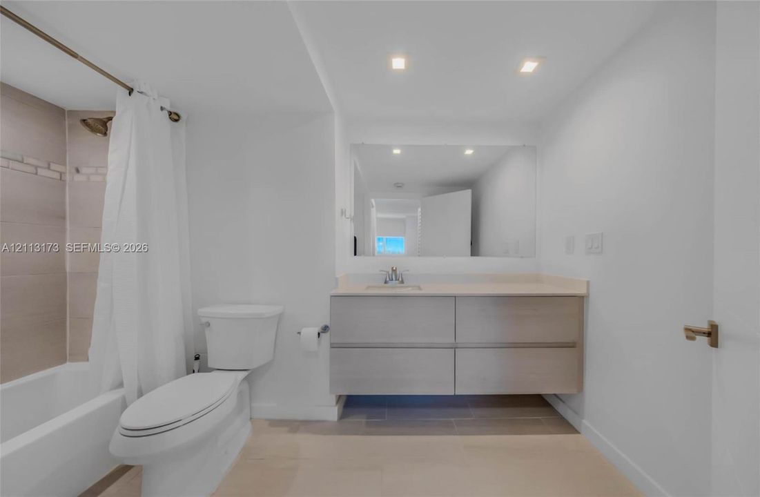 Floating vanity featuring a solid surface countertop, rectangular undermount sink, large wall-mounted mirror, recessed ceiling lighting, and tile shower surround