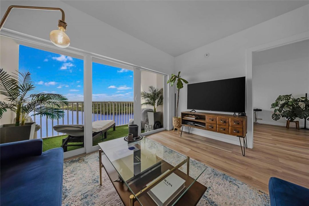 Floor-to-ceiling windows, wood-finish flooring, and a private balcony with metal railing