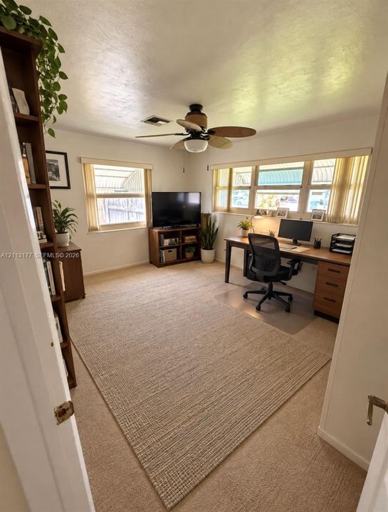 Room featuring neutral wall-to-wall carpeting, abundant natural light from multi-pane windows, and a ceiling-mounted light fixture with a five-blade fan