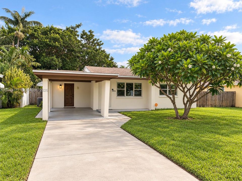 Exterior facade featuring a covered carport, concrete driveway, and expansive lawn with mature landscaping