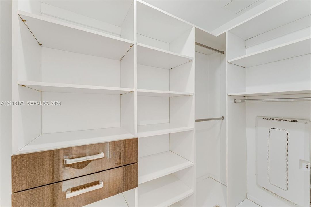 Custom reach-in closet featuring white adjustable shelving, two integrated drawers with wood-finish fronts, metal hardware, and dual hanging rods