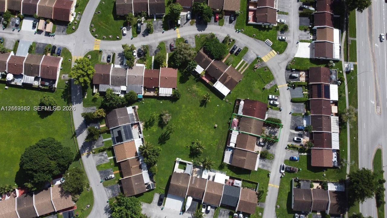 Aerial perspective of a residential community featuring structured asphalt roadways, manicured communal green spaces, mature shade trees, and paved off-street parking