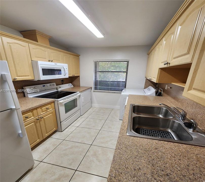 Kitchen featuring light-finish cabinetry, speckled countertops, dual-basin stainless steel sink, tile flooring, and integrated white appliances