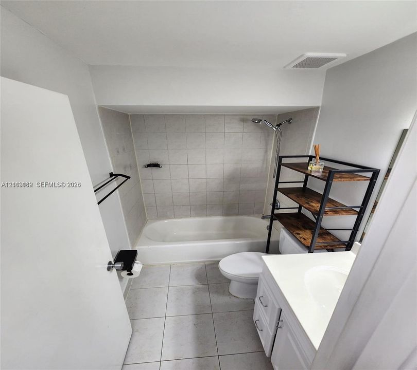 Bathroom featuring tile flooring, a shower-tub combination with tiled surround, an integrated vanity with a solid-surface countertop, and matte black hardware