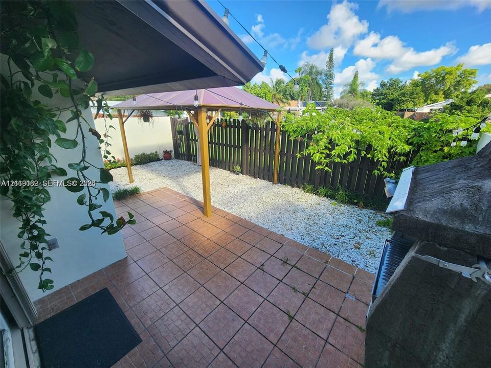 Tiled patio featuring a metal-framed gazebo, gravel landscaping, a privacy fence, and integrated string lighting