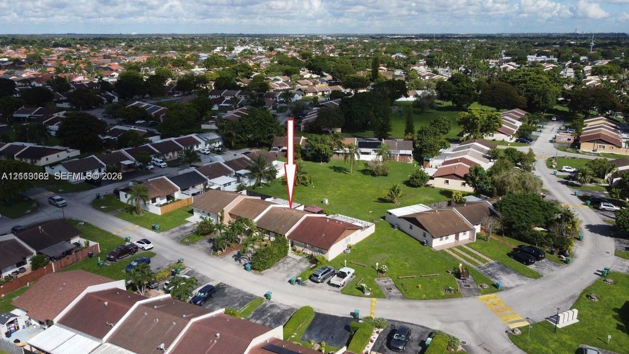 Aerial perspective of a multi-unit property featuring a neutral exterior finish, a pitched roofline, and an expansive rear lawn