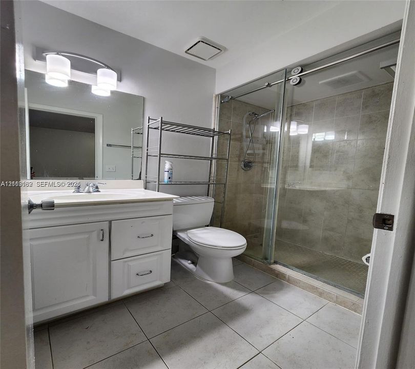 Bathroom featuring a white vanity with integrated sink, walk-in shower with glass enclosure and neutral-toned wall tile, and tile flooring