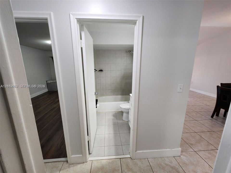 Bathroom featuring a white bathtub, tile wall surround, and light-toned floor tiling, alongside wood-finish flooring in the exterior space and tile flooring in the room