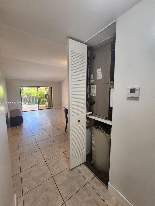 Utility closet featuring a louvered bifold door, an HVAC air handler unit, and a water heater, with ceramic tile flooring extending throughout the interior space