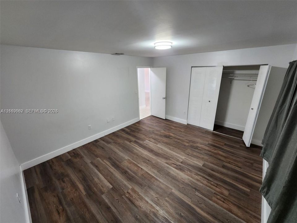 Room featuring wood-finish flooring, neutral wall paint, overhead flush-mount lighting, and a closet with bifold doors