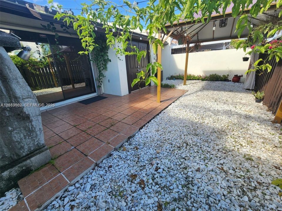 Enclosed courtyard featuring terra-cotta tile flooring, white stone ground cover, a built-in pergola, and sliding glass doors
