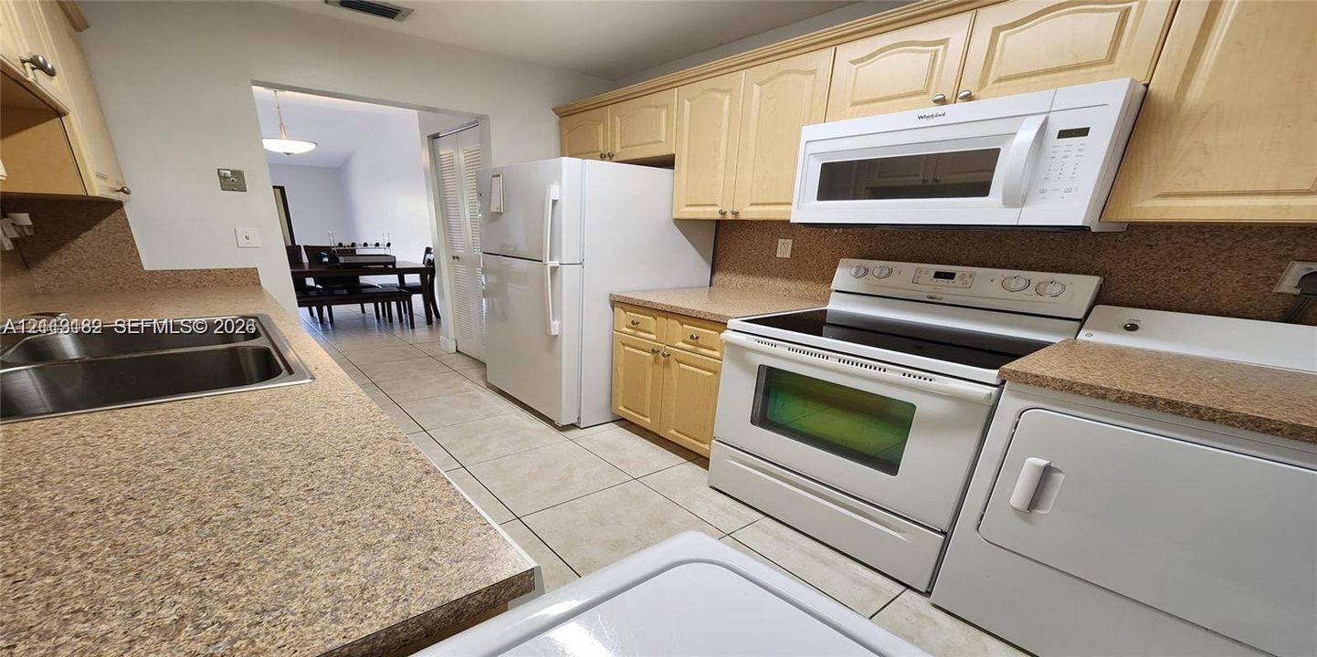 Kitchen featuring light-finish cabinetry, speckled countertops, dual-basin stainless steel sink, and white appliances including a built-in microwave and range