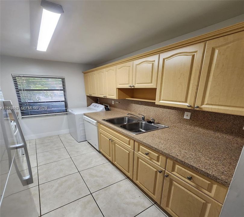 Laundry room featuring extensive light wood cabinetry, stone-composite countertops, dual-basin stainless steel sink, large-format ceramic tile flooring, and integrated overhead lighting