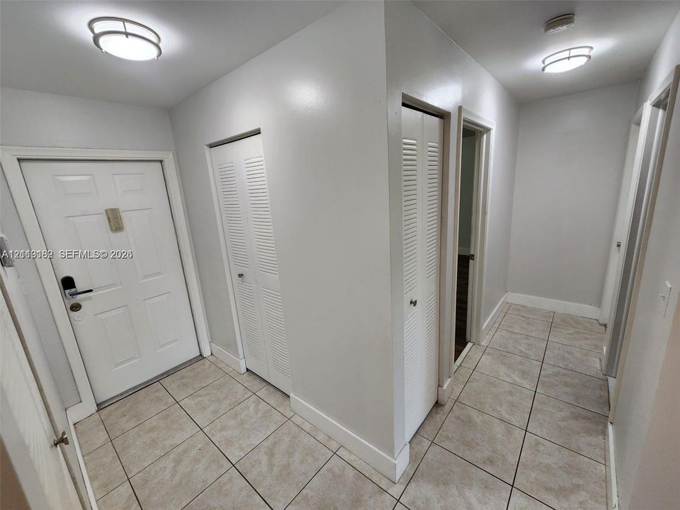 Entryway featuring neutral tile flooring, two louvered-panel closets, flush-mount ceiling lighting, and a multi-panel door with metallic hardware