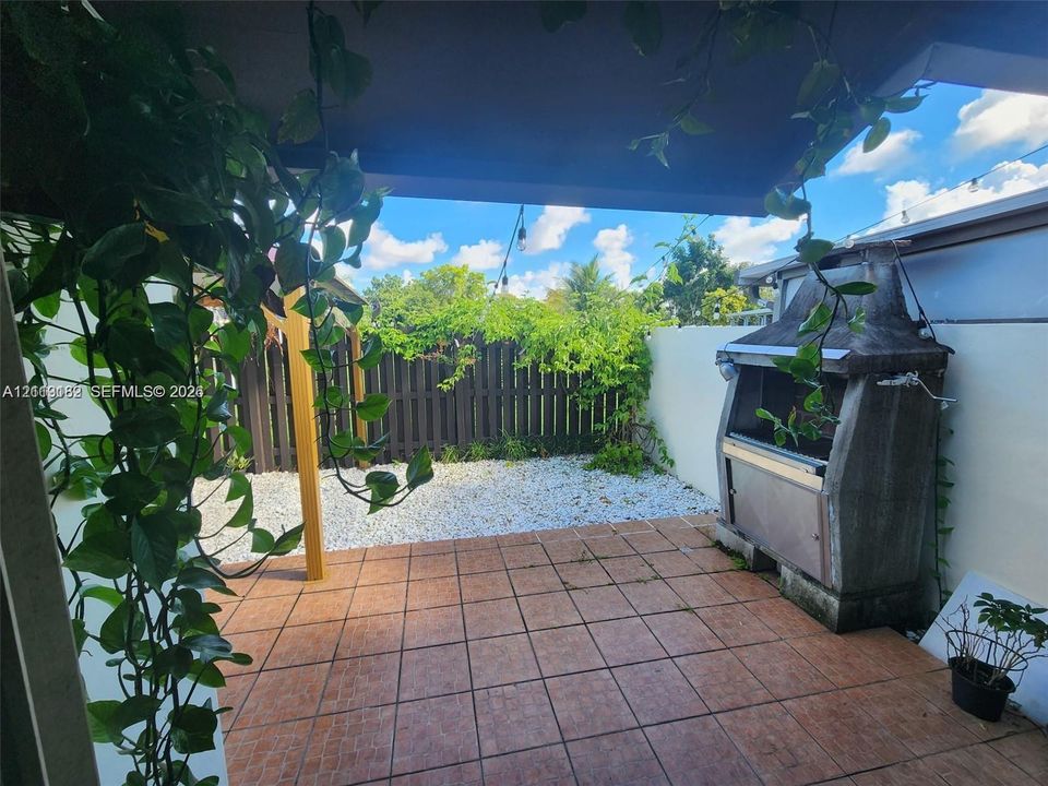 Covered patio with tiled flooring, built-in masonry grill, and fenced backyard with stone ground cover