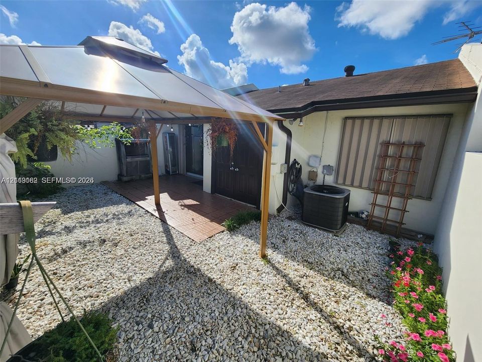 Enclosed backyard featuring a hard-top gazebo, paved patio area, stone ground cover, and exterior wall-mounted shutter system