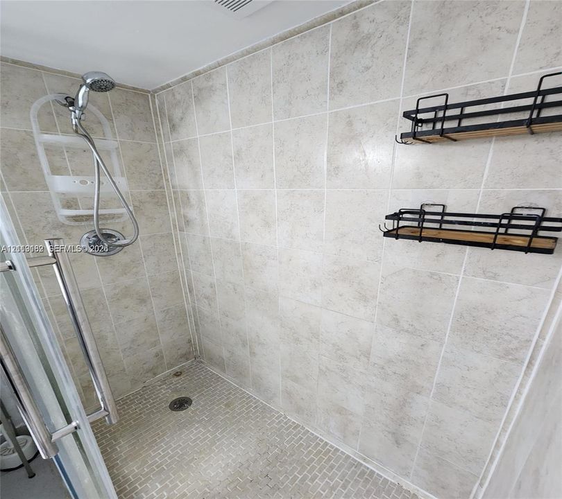 Walk-in shower featuring light-toned large-format wall tile, a mosaic-tiled floor, chrome hand-held shower fixture, and metal-framed glass enclosure