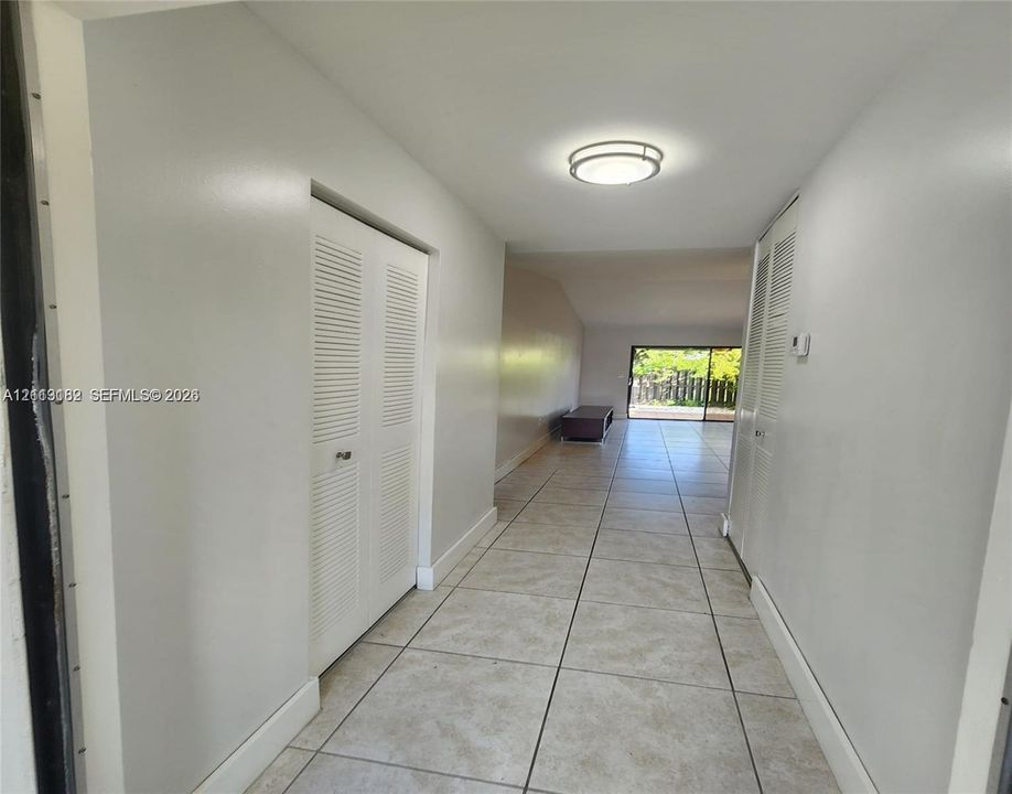 Neutral-toned interior featuring large-format tile flooring, double-door louvered closets, a flush-mount ceiling light fixture, and sliding glass doors