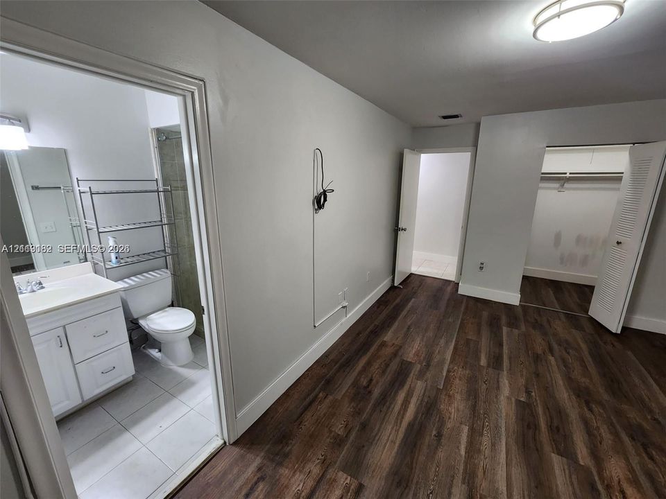 Wood-finish flooring throughout, walk-in closet with louvered doors, and full bathroom featuring a white vanity cabinet and tile flooring