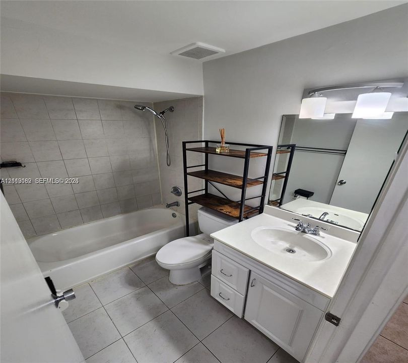 Bathroom featuring a white vanity with an integrated sink, a tiled shower-tub combination, a large rectangular wall-mounted mirror, and multi-bulb vanity lighting