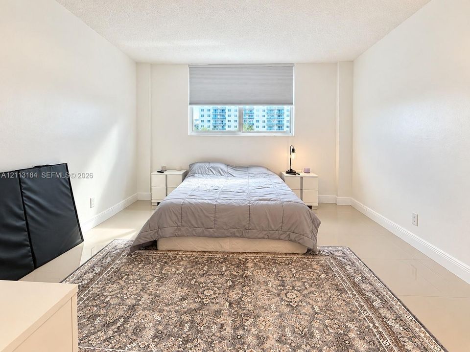 Neutral-toned interior featuring smooth wall finishes, large-format tile flooring, and a window with an integrated roller shade