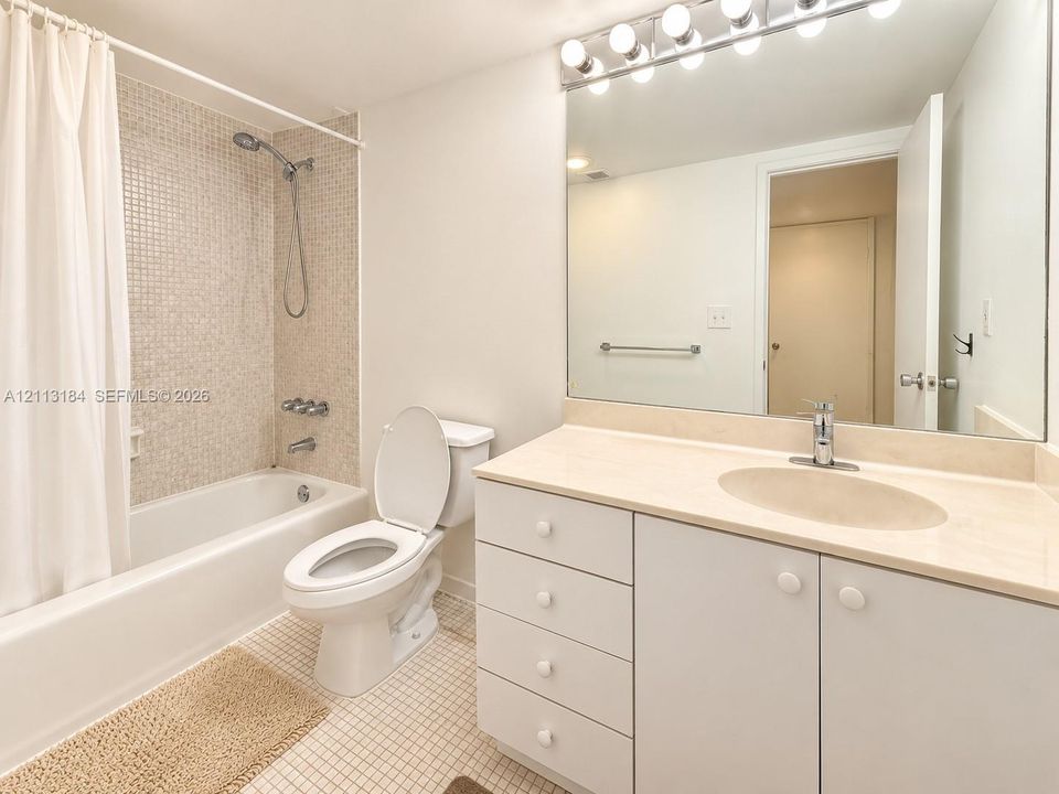 Bathroom featuring a vanity with integrated sink and countertop, a large wall-mounted mirror, overhead multi-bulb lighting, and a bathtub with mosaic tile surround and handheld shower fixture