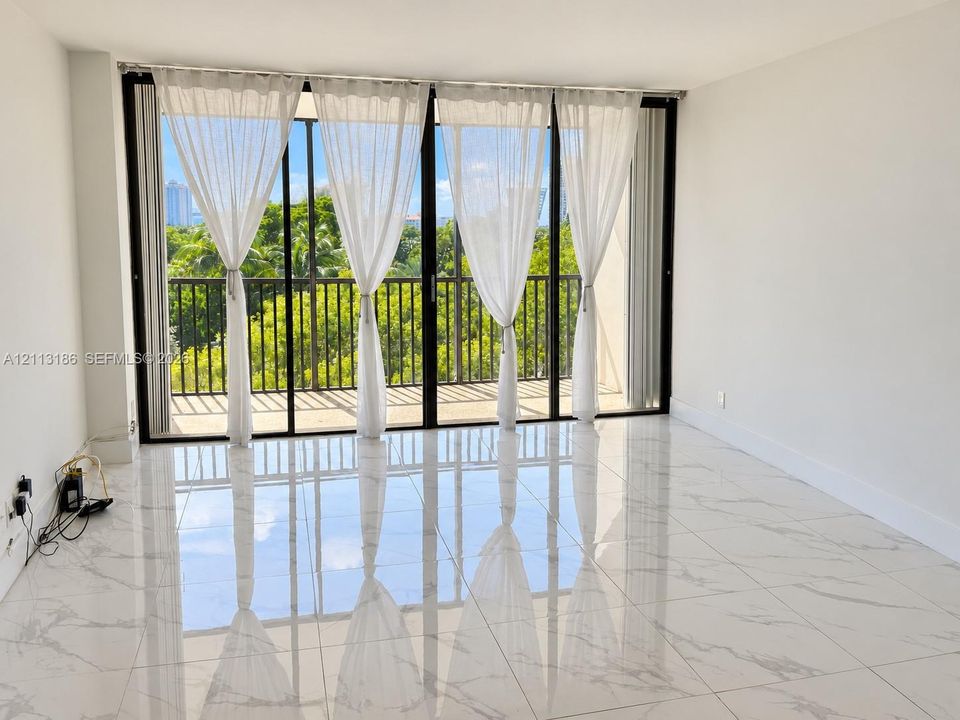 Large format polished stone-finish flooring, floor-to-ceiling sliding glass doors, and a private balcony with black metal railing