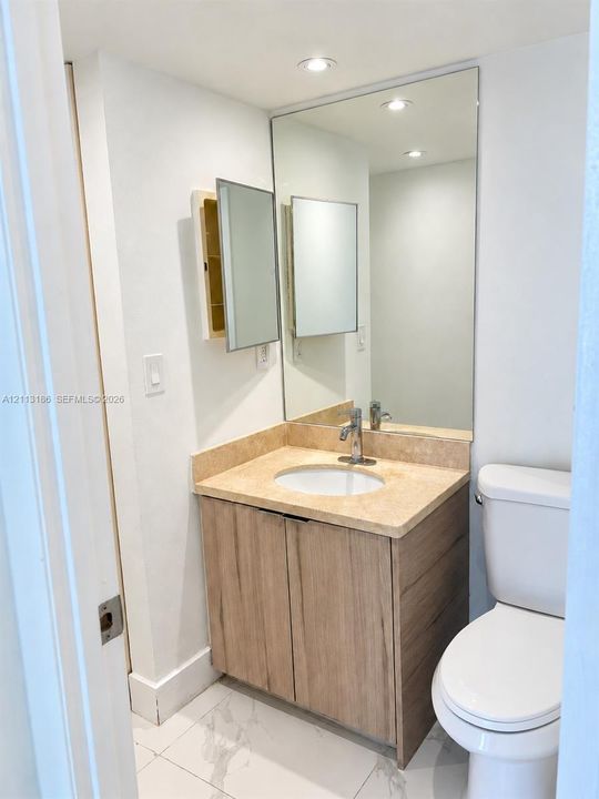 Vanity with wood-finish cabinetry, stone countertop, integrated sink, recessed lighting, and large wall-mounted mirror