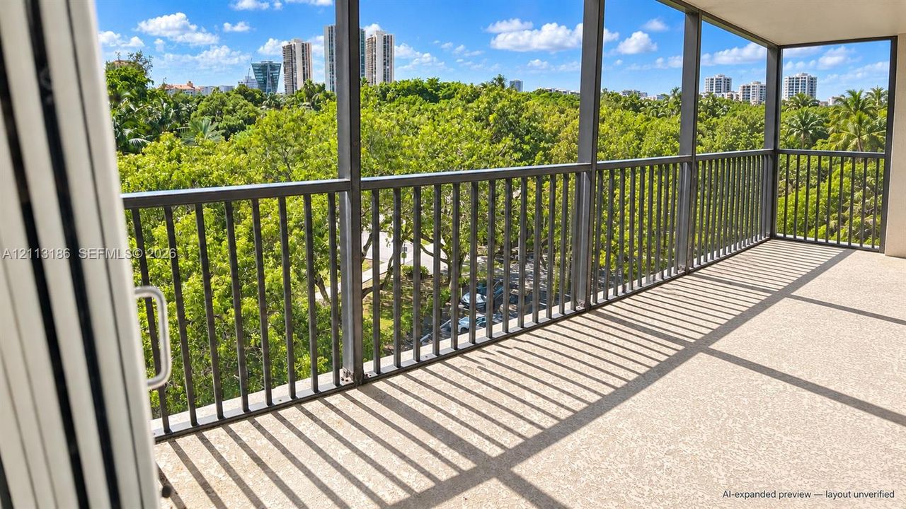 Screened-in balcony featuring metal railing, concrete flooring, and panoramic urban and tree-lined scenery