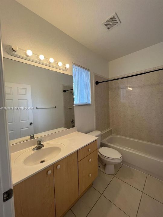 Bathroom featuring a vanity with light-wood cabinetry, white solid-surface countertop, integrated basin, wall-mounted mirror, and tile flooring