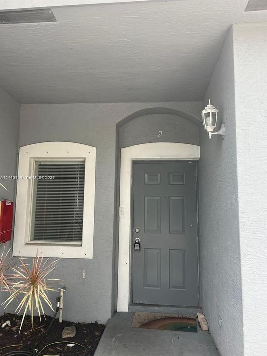 Covered entryway featuring a solid-panel door with arched molding, recessed window with white trim, and a wall-mounted coach lantern