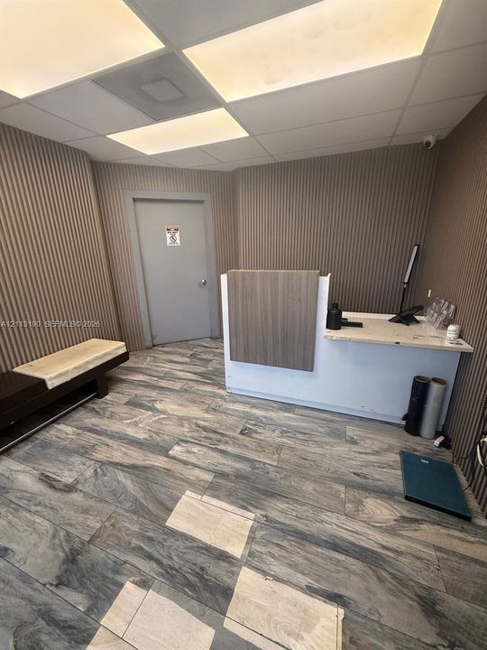 Reception area featuring vertically paneled walls, stone-patterned tile flooring, built-in reception desk with a light-toned countertop, and recessed panel lighting