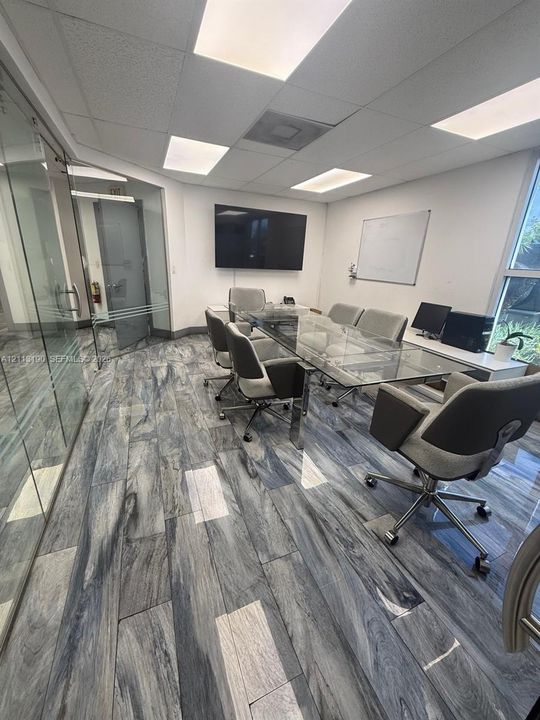 Conference room featuring full-height glass walls, wood-finish tile flooring, recessed drop-ceiling lighting, and a wall-mounted whiteboard