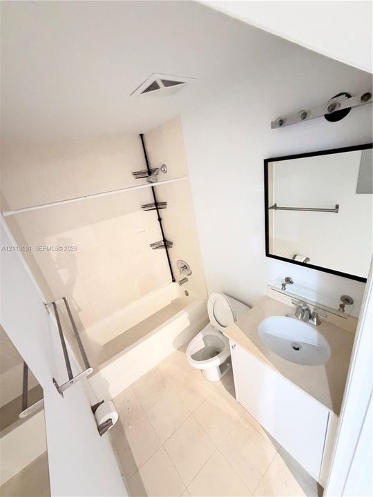 Bathroom featuring a porcelain tub and shower combination, white vanity with an integrated basin, framed wall mirror, and neutral tile flooring