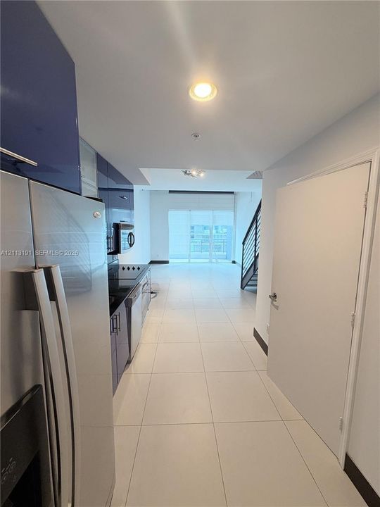 High-gloss blue cabinetry, stainless steel appliances, large-format tile flooring, recessed lighting, and a metal staircase railing