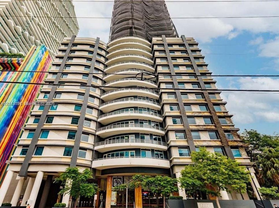 High-rise architectural exterior featuring tiered balconies, expansive glass window walls, concrete structural columns, and a multi-story facade design
