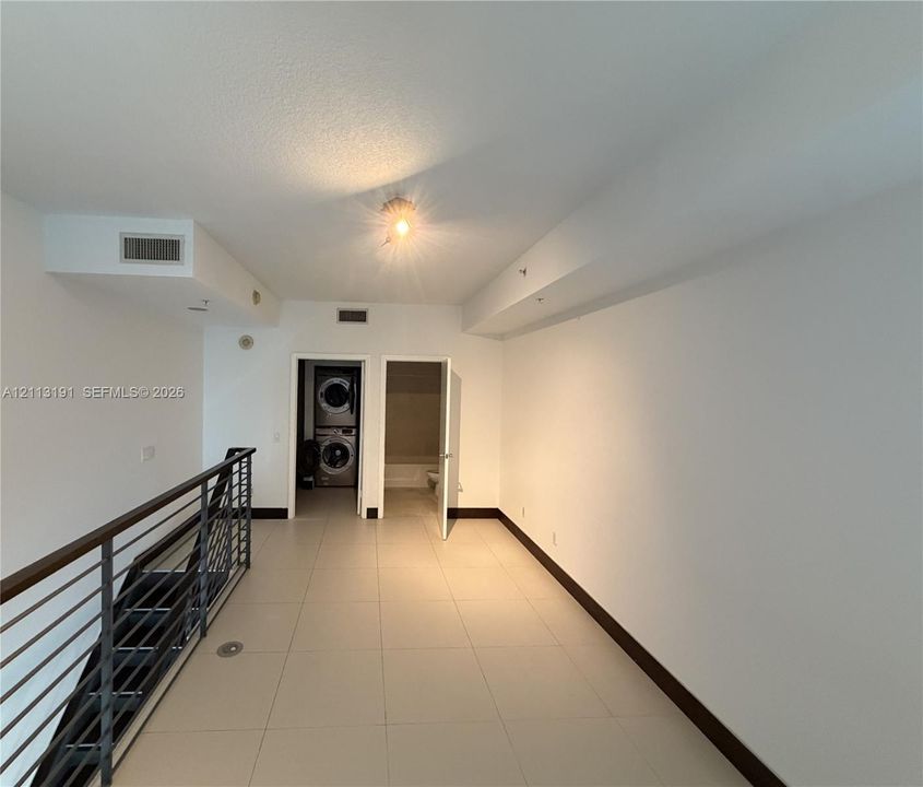 Staircase featuring a metal railing with a dark handrail, neutral ceramic tile flooring, and dedicated laundry area with a stackable appliance unit
