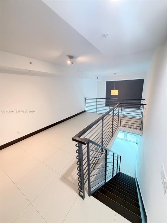 Open-concept interior featuring large-format tile flooring, metal horizontal-bar railings, dark-finish staircase treads, and a suspended pendant light fixture