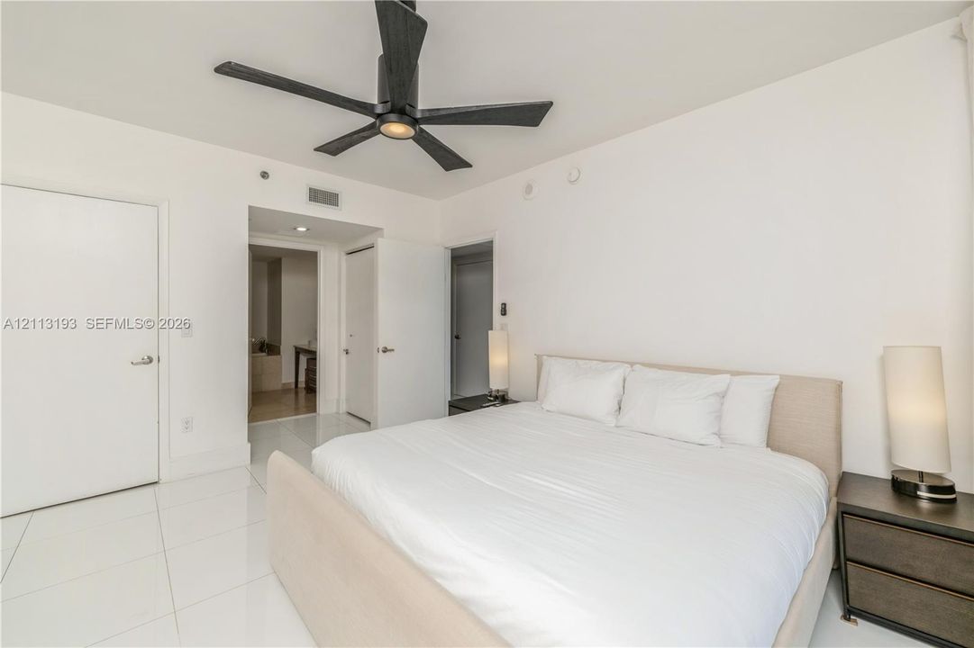 Interior room featuring polished white tile flooring, matte black ceiling fan with integrated lighting, and white smooth-finish interior doors