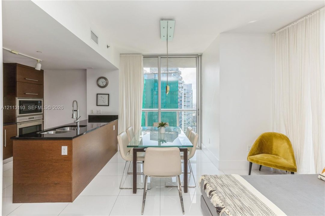Kitchen featuring dark wood-finish cabinetry, black stone countertops, and built-in stainless steel appliances, paired with high-gloss tile flooring and floor-to-ceiling glass doors opening to an exterior balcony